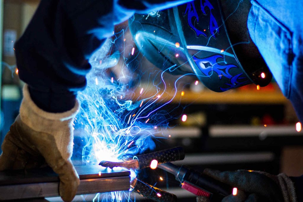 Welding school student wearing a welding mask and working with sparks and blue smoke rising